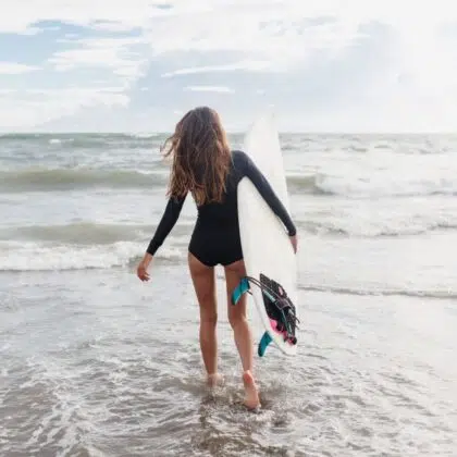 activités nautiques sables d'olonne 12 Young sporty active woman dressed swimsuit runs in the ocean with surf board in sunny day. Surfer girl walking with board on the sandy beach.
